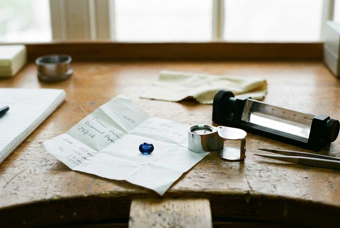 An oval sapphire on diamond paper beside a loupe and refractometer